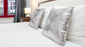 Ein Hotelzimmer mit einem Bett, zwei Kissen, einem Nachttisch mit Lampe und einem Fenster mit Vorhängen.