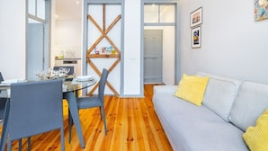 A modern living room with a grey sofa, wooden flooring, and a dining area with a glass table and chairs. - Lisbon Prime Aparts - Prata (Lisboa)