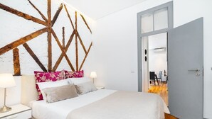 A bedroom with a bed, nightstands, a wooden wall feature, and a door leading to another room. - Lisbon Prime Aparts - Prata (Lisboa)