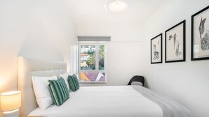 A bedroom with a bed, a nightstand, a lamp, a chair, and framed artwork on the wall.
