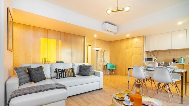 A modern living room with a white sofa, a dining area with a table set for two, and a kitchen in the background.