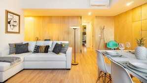 A modern living room with a white sofa, a dining table set for two, and a wooden floor.