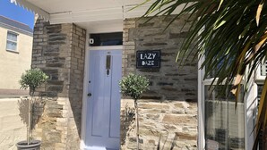 Ein Steinhaus mit einer weißen Tür, zwei Topfpflanzen und einem Schild mit der Aufschrift 'LAZY DAZE'.