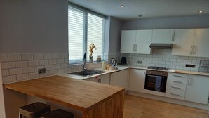 Eine moderne Küche mit einer Holztischinsel, zwei Barhocker, einem Einbauofen und einem Fenster mit Jalousien.