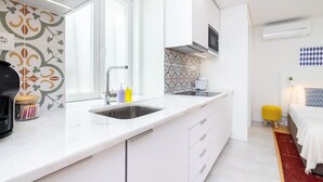 A modern kitchen with white cabinets, a double sink, and a built-in oven. There is a window providing natural light and a TV mounted above the oven. - Lisbon Prime Aparts - Baixa (Lisboa)