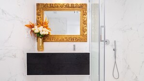 A bathroom with a marble wall, a gold-framed mirror, a black vanity, and a shower area.