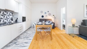 Une cuisine moderne avec des meubles blancs, un plan de travail en marbre et un coin repas comprenant une table et des chaises en bois.