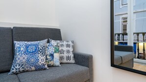 A grey sofa with patterned cushions and a mirror reflecting a building. - Lisbon Prime Aparts - Baixa (Lisboa)