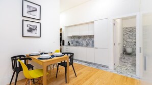 A modern kitchen with white cabinets, a marble backsplash, and a wooden dining table with yellow chairs. - Lisbon Prime Aparts - Baixa (Lisboa)
