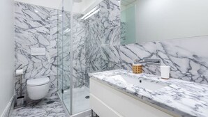A modern bathroom with a glass shower enclosure, a marble-tiled shower area, and a white sink with a marble countertop. - Lisbon Prime Aparts - Baixa (Lisboa)