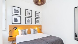 A neatly arranged bedroom with a large bed, a wooden headboard, and a series of framed pictures on the wall. - Lisbon Prime Aparts - Baixa (Lisboa)