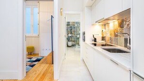 A narrow hallway leading to a modern kitchen with white cabinets, a stainless steel sink, and a tiled backsplash. - Lisbon Prime Aparts - Baixa (Lisboa)