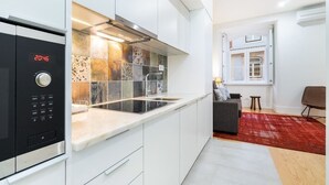 A modern kitchen with white cabinetry, a black induction cooktop, and a backsplash with multicolored tiles. - Lisbon Prime Aparts - Baixa (Lisboa)