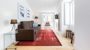 Una sala de estar moderna con un sofá marrón, una mesa de centro de vidrio, una alfombra roja y un televisor montado en la pared.