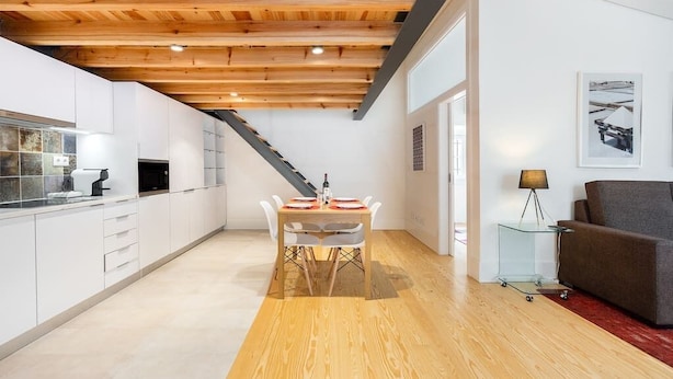 Una cocina moderna con armarios blancos, techo de madera y un comedor con mesa y sillas.