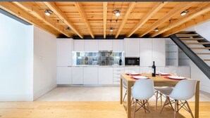 Una cocina moderna con armarios blancos, techo de madera y comedor con una mesa dispuesta para cuatro.