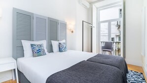 A bedroom with a large bed, grey shutters, a white nightstand, and a view of the outside balcony. - Lisbon Prime Aparts - Baixa (Lisboa)