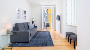 A modern living room with a grey sofa, a blue rug, and a glass coffee table. There are framed pictures on the wall and a lamp on a side table. - Lisbon Prime Aparts - Baixa (Lisboa)
