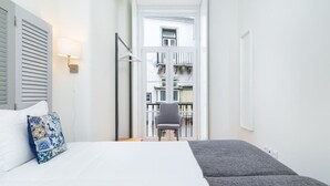 A narrow hotel room with a bed, a chair, and a view of an outdoor balcony. - Lisbon Prime Aparts - Baixa (Lisboa)