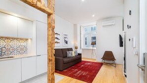 A modern kitchen with white cabinets and a patterned backsplash, a brown sofa with cushions, a red rug, and a wooden floor. - Lisbon Prime Aparts - Baixa (Lisboa)