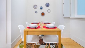 A dining area with a wooden table set for four, white chairs, and a variety of decorative plates on the wall. - Lisbon Prime Aparts - Baixa (Lisboa)