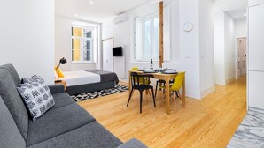 A modern living room with a grey sofa, a dining table with yellow chairs, and a wooden floor. - Lisbon Prime Aparts - Baixa (Lisboa)