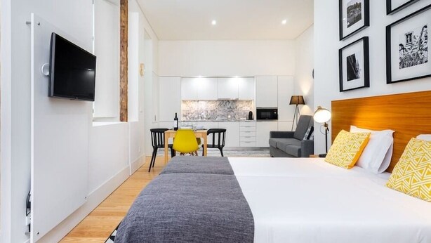 A modern hotel room with a large bed, a desk, and a kitchenette in the background. - Lisbon Prime Aparts - Baixa (Lisboa)