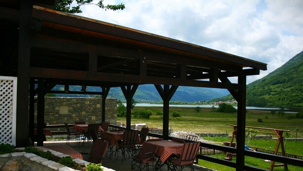 Un patio al aire libre con mesas y sillas, un muro de piedra y vistas a un lago y montañas.