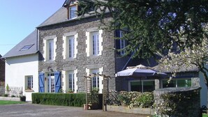 Un bâtiment en pierre doté d’un toit en pente, de nombreuses fenêtres et d’un jardin bien entretenu où poussent une grande variété de plantes et de fleurs.