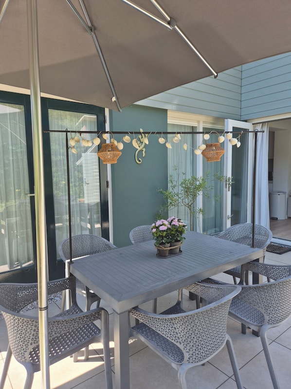 An outdoor patio with a table and chairs, a hanging light fixture, and a potted plant.