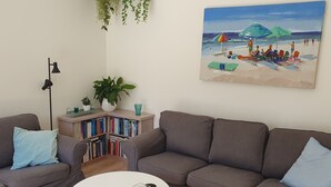 Una sala de estar con dos sofás, una estantería, una mesa de centro y un cuadro de una playa.