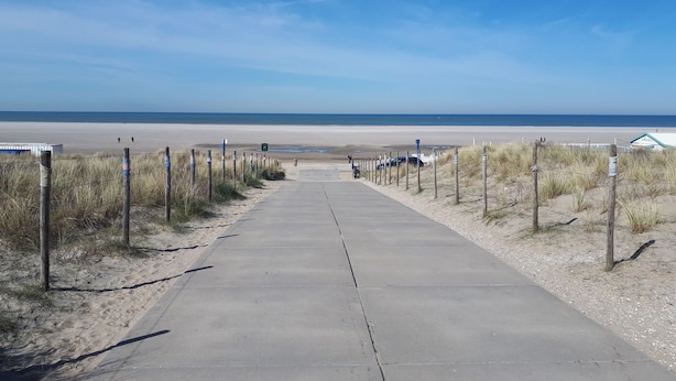 Un sendero de hormigón que conduce a una playa, con una valla en un lado y un edificio en el otro.