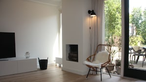 Un salón moderno con televisor de pantalla plana, chimenea, sillón de mimbre y un ventanal con vistas al exterior.