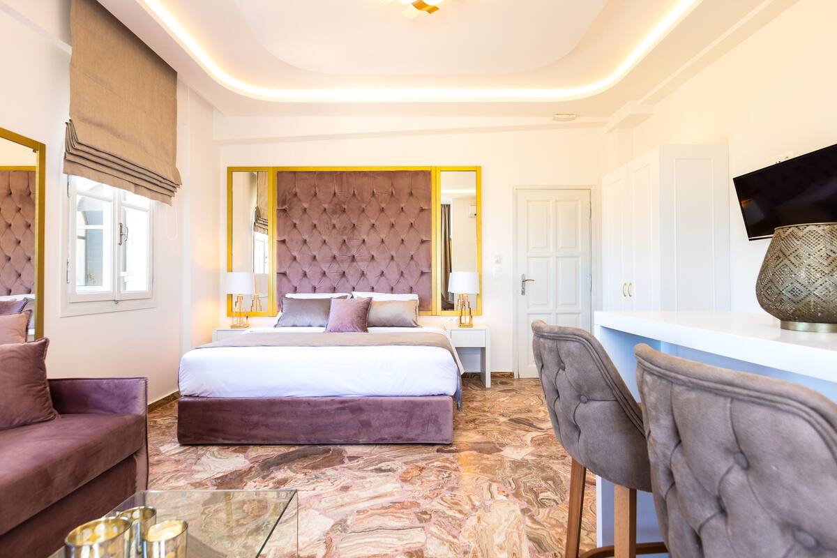 Ein modernes Hotelzimmer mit einem großen Bett, einer Sitzecke mit Sofa und Sessel, einem Schreibtisch und einem Fernseher.
