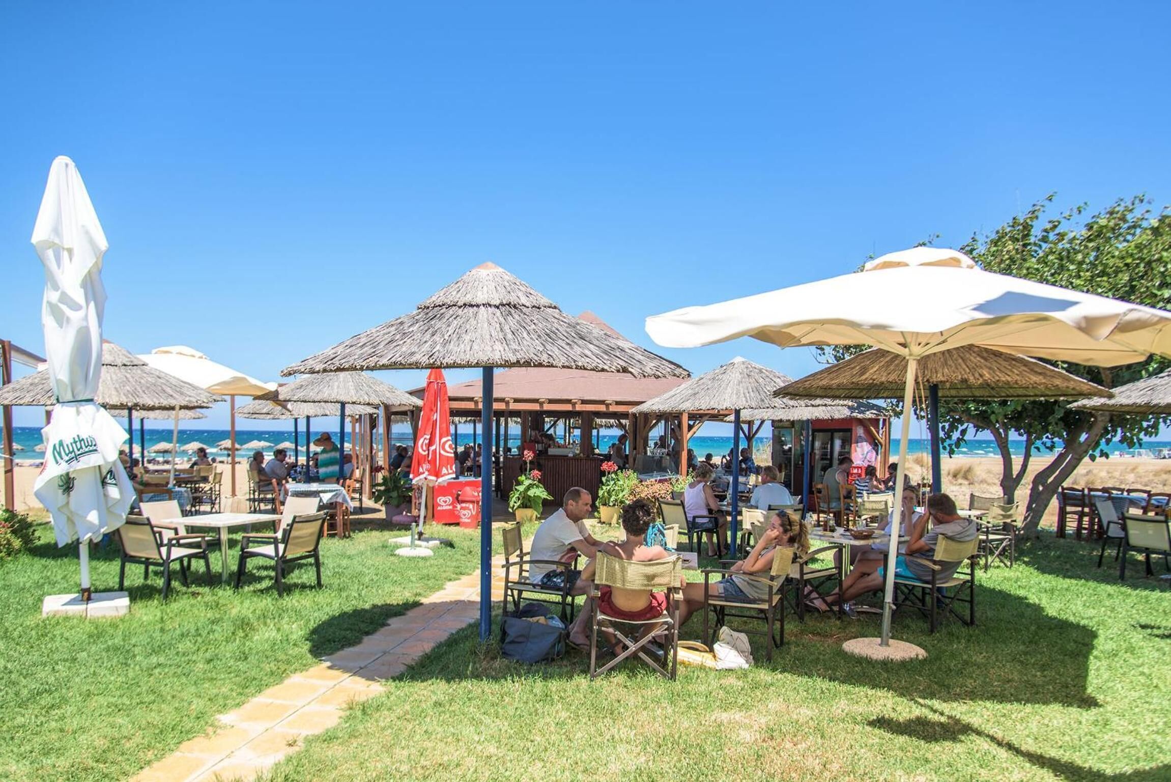 Un espace de restauration en plein air, avec des tables et des chaises disposées sous des parasols en chaume, offrant une vue sur la mer.