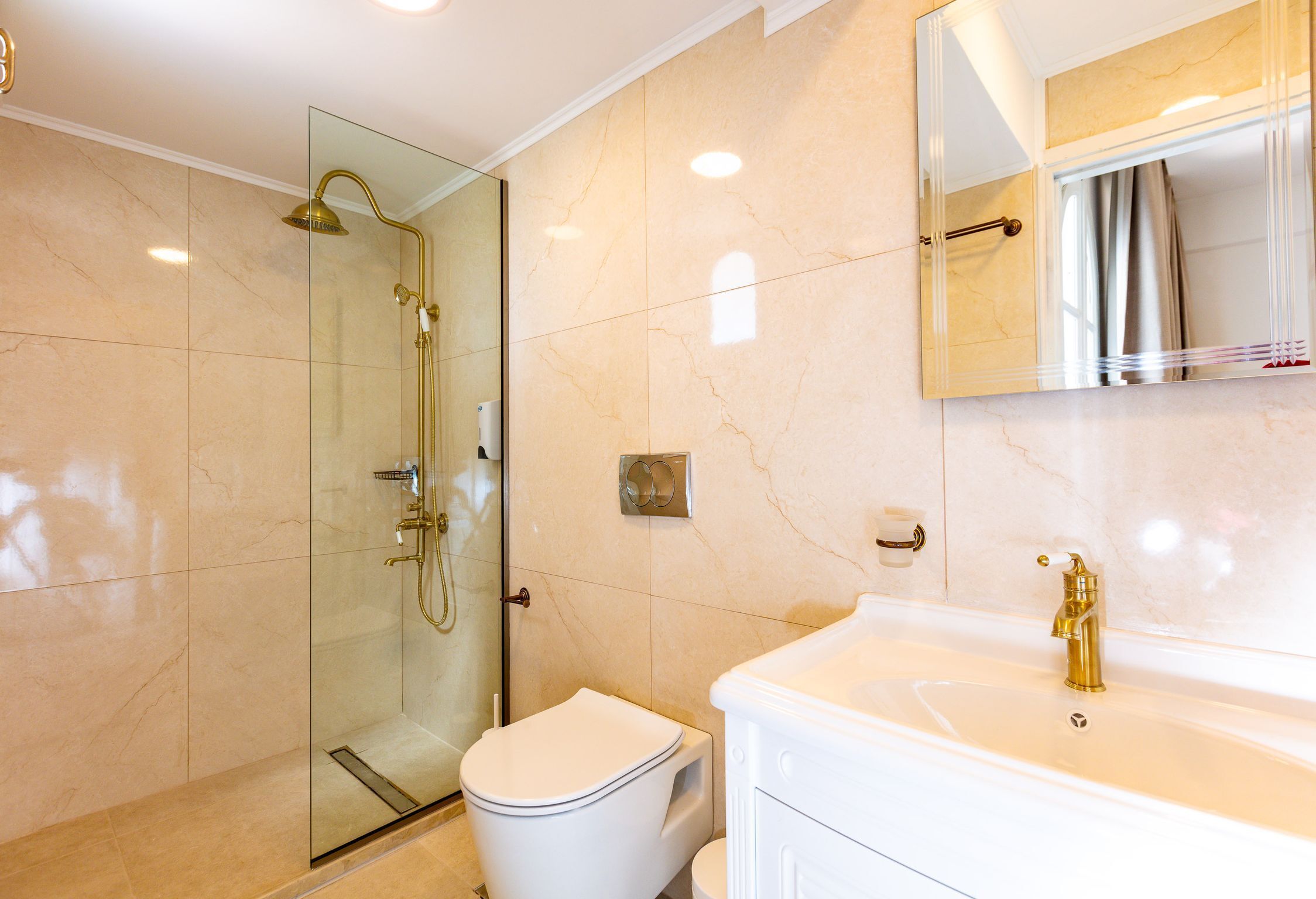 Une salle de bain moderne avec une douche à parois de verre, des toilettes blanches et un lavabo blanc agrémenté de robinetterie dorée.
