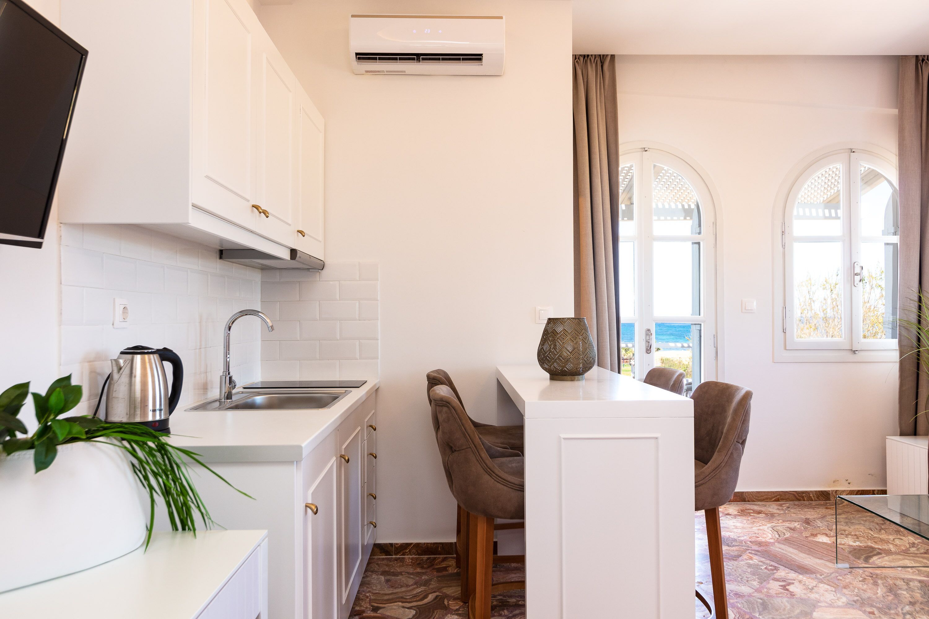 A modern kitchen with white cabinets, a stainless steel kettle, and a glass table.