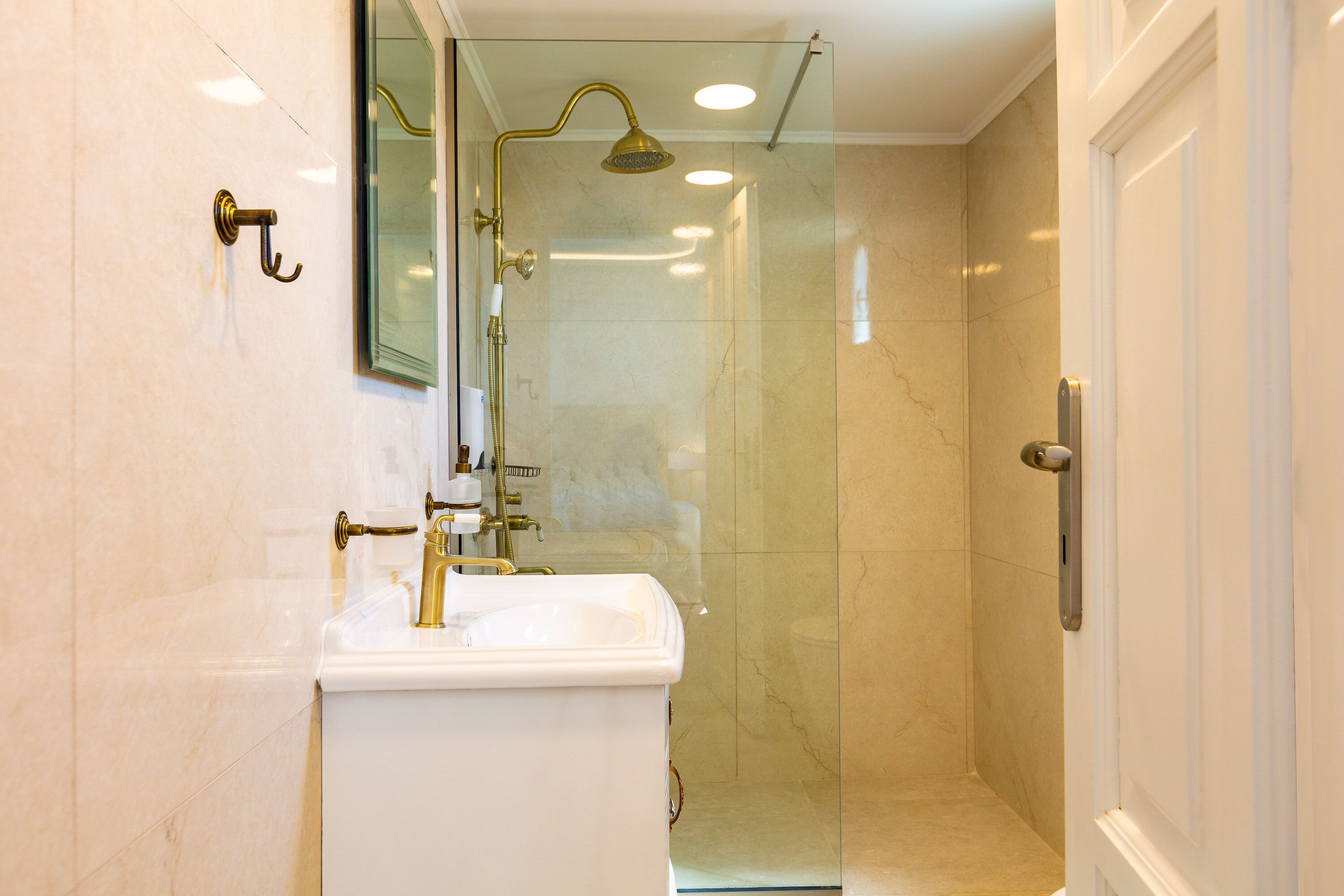 Un baño con lavamanos blanco, detalles dorados y ducha con cerramiento de vidrio.
