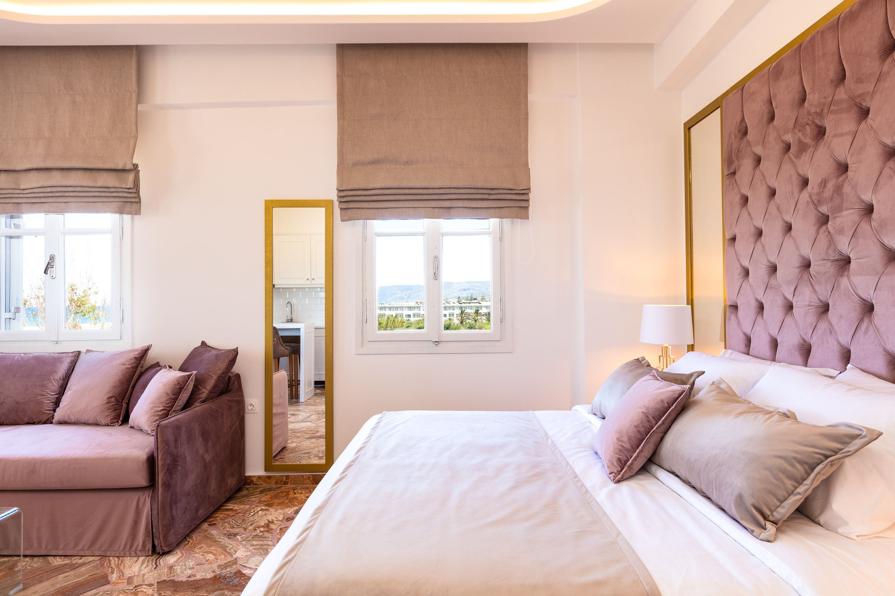 Habitación de hotel con cama, sofá, un espejo grande y vistas al exterior.