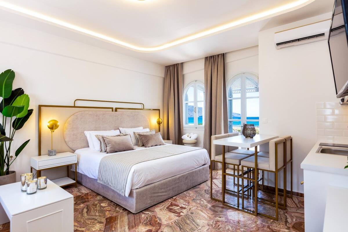 Ein modernes Schlafzimmer mit einem großen Bett, Nachttischen, einem Schreibtisch und Blick auf das Meer.