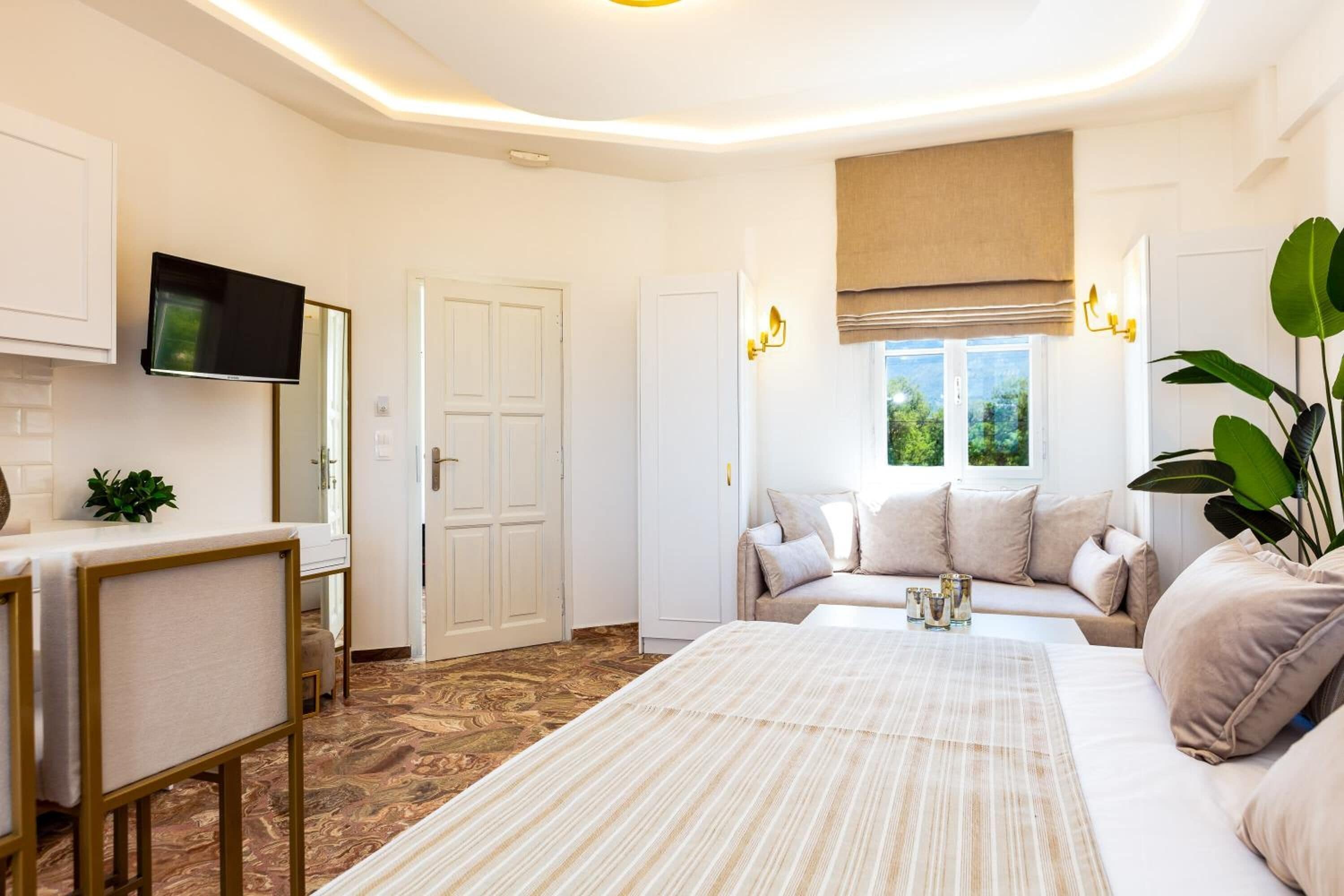 Quarto moderno com uma cama grande, um sofá, uma televisão na parede e uma janela com vista para vegetação.