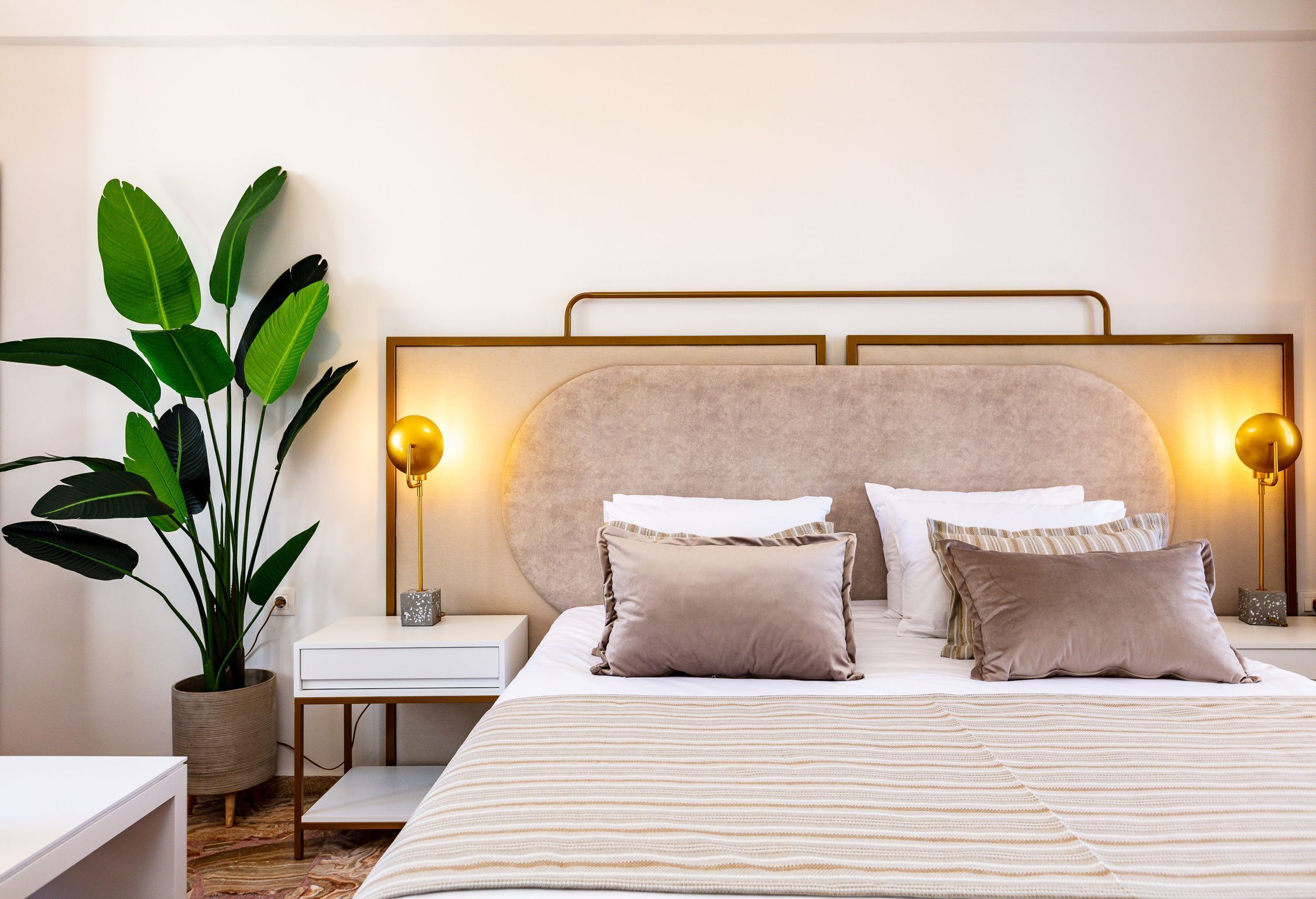 Un dormitorio ordenado con cama, mesitas de noche, lámpara y una planta en maceta.