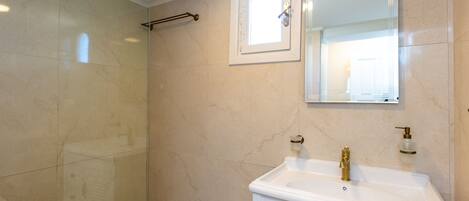 A bathroom with a glass shower enclosure, a white sink with gold fixtures, and a mirror above the sink.