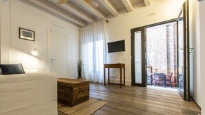 Un accogliente soggiorno con pavimento in legno, un divano bianco, un settimino in legno, un tavolino e una televisione a parete.