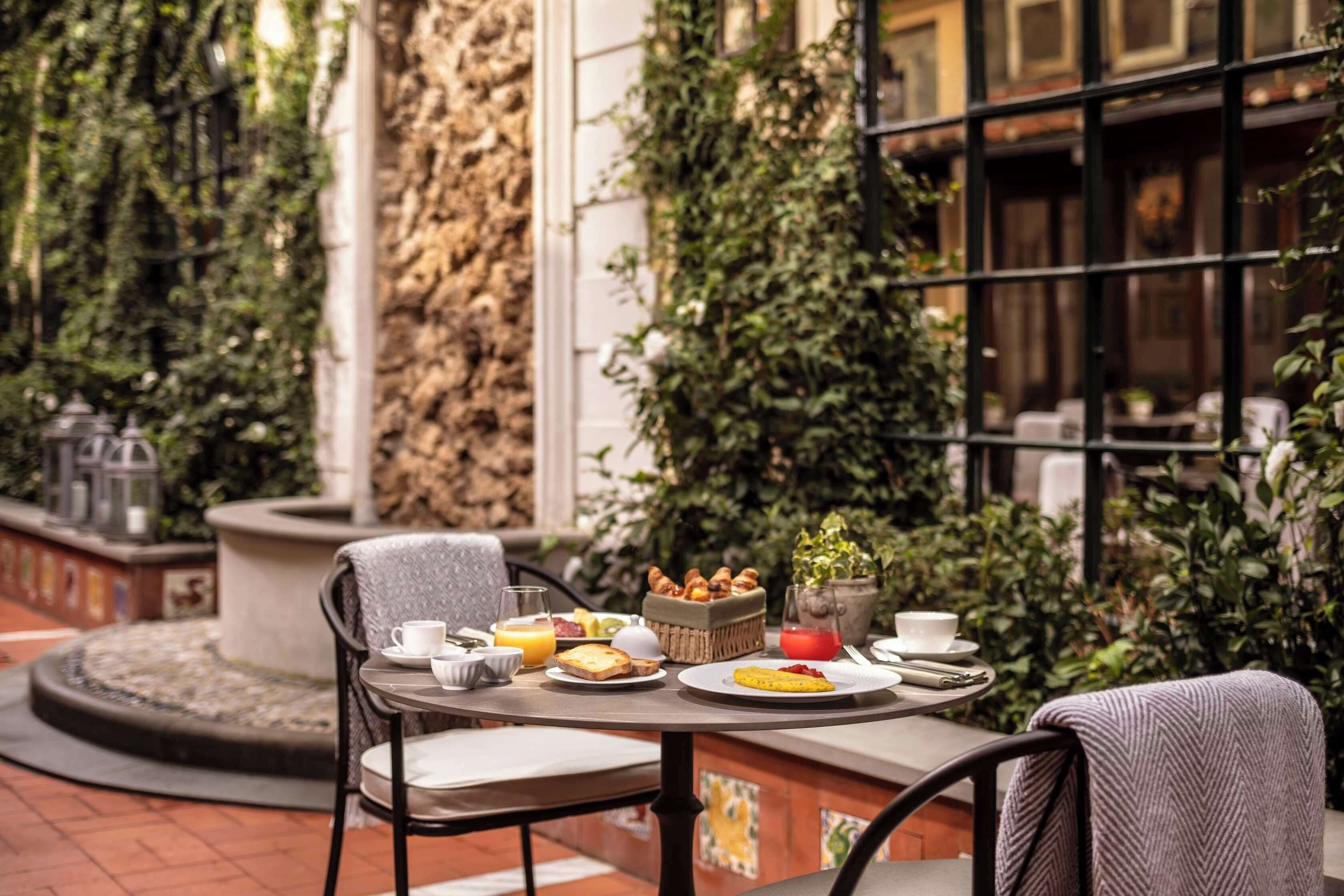 Un caffè all'aperto con un tavolo rotondo, sedie e una selezione di prodotti per la colazione.