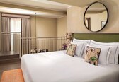 A hotel room with a large bed, a round mirror, a balcony with curtains, and a staircase.