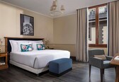 A hotel room with a large bed, a chair, a table, and a window with curtains.