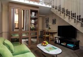 A living room with a green sofa, a coffee table with a book, a TV, and a staircase.