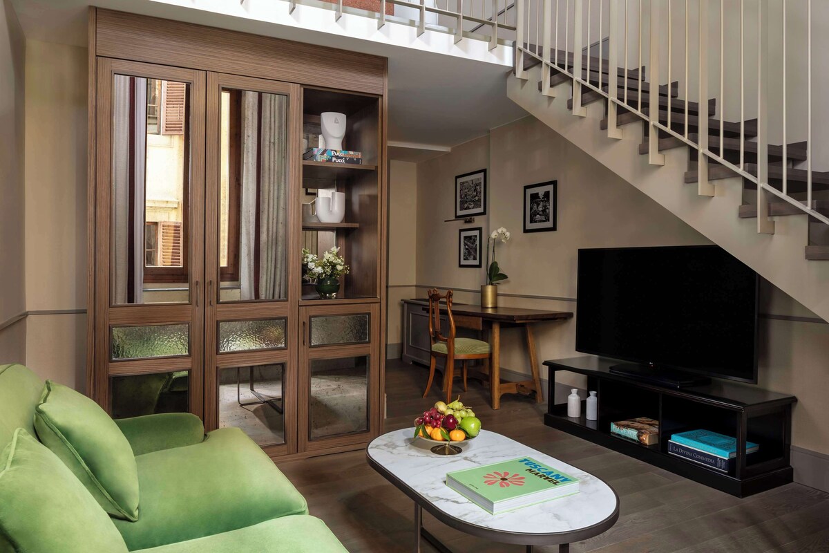 A living room with a green sofa, a coffee table with a book, a TV, and a staircase.