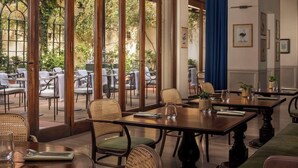 A restaurant with wooden tables and wicker chairs, large windows with a view of trees, and framed artwork on the walls. - Tivoli Palazzo Gaddi Firenze Hotel (Florence)